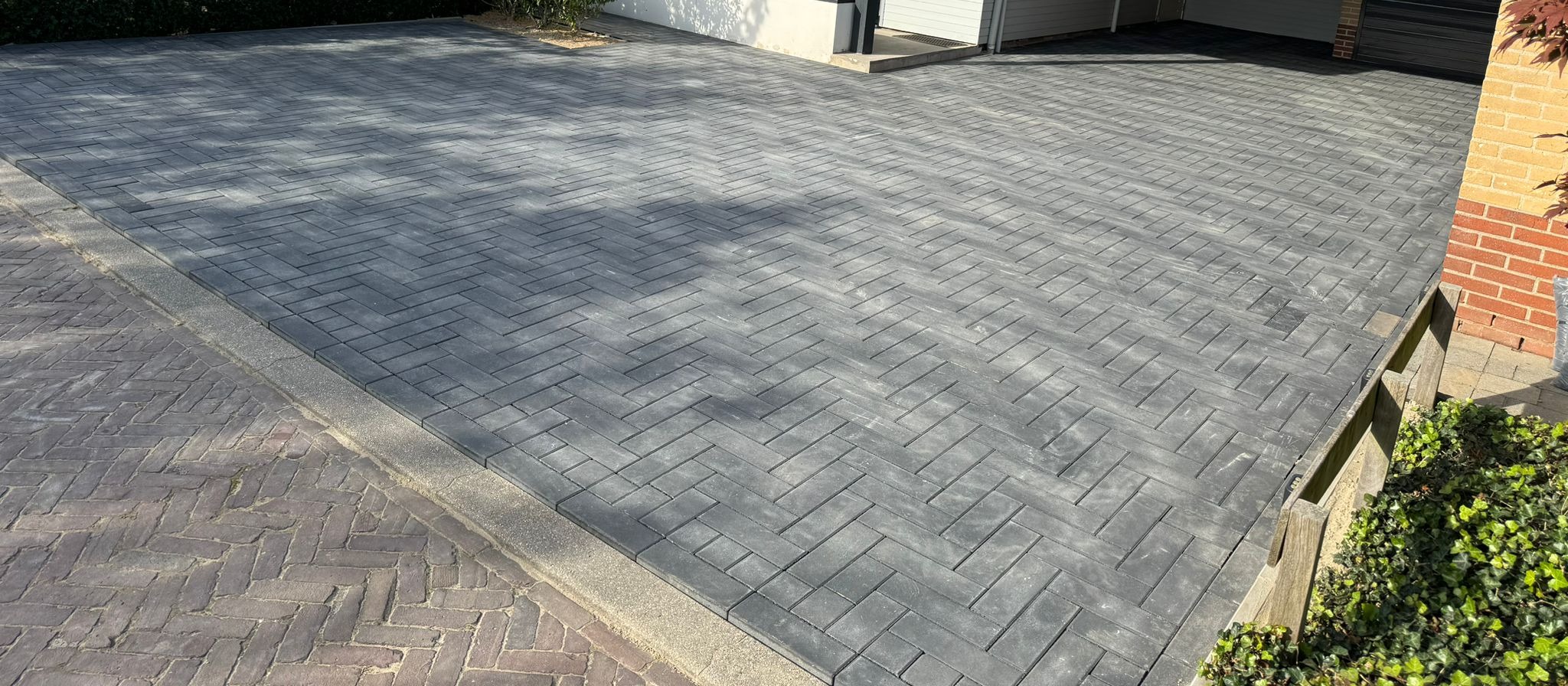 Grote oprit in antraciet klinkers in keperverband, met opsluitbanden en een carport