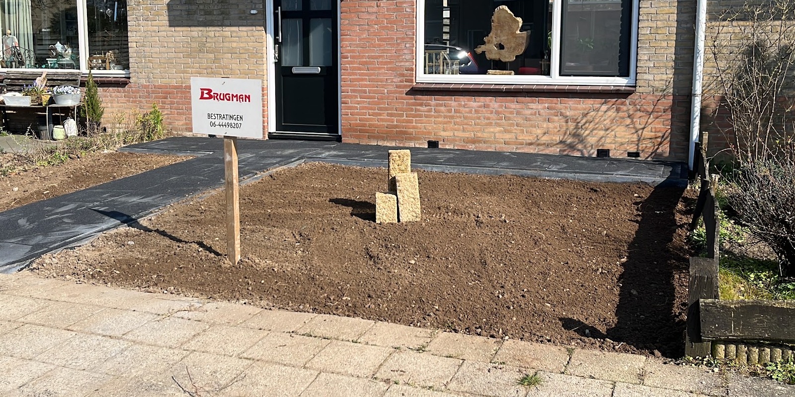 Voortuin van een rijtjeshuis met een geëgaliseerde ondergrond, een nieuw pad en het bord van Brugman Bestratingen